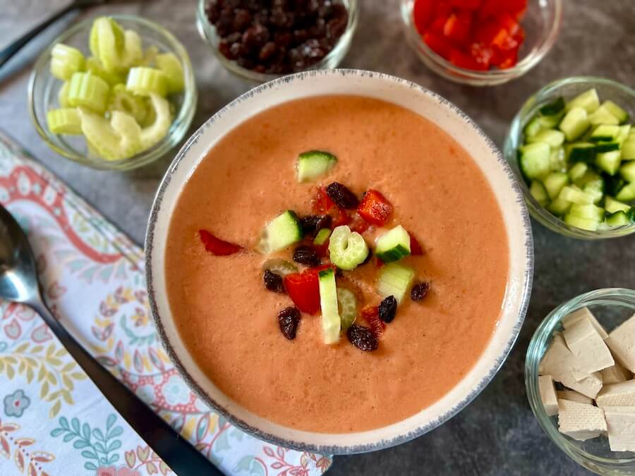 Bowl of authentic Spanish gazpacho with raisins and finely chopped pepper and cucumber on top