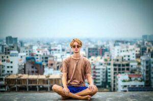 Man meditating cross legged with cityscape behind