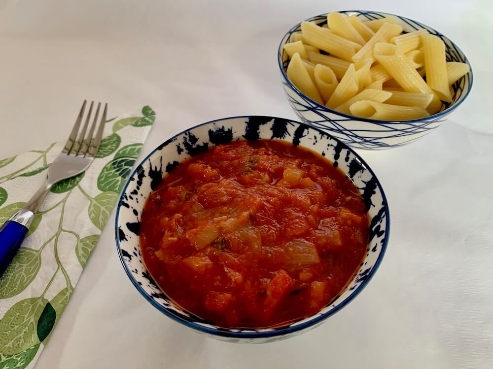 Bowl of tomato sauce with a bowl of pasta in the background