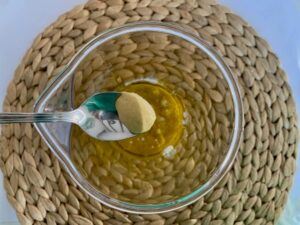 Half a teaspoon of mustard over a container holding the ingredients of vegan mayonnaise