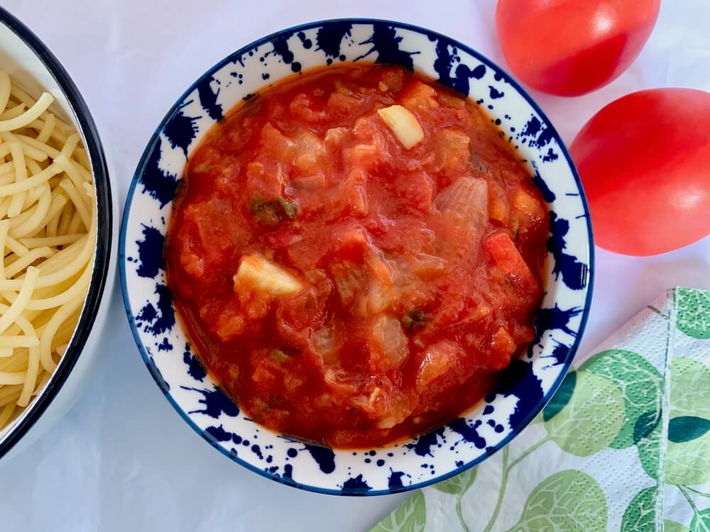 Bowl of tomato sauce with tomatoes in the background