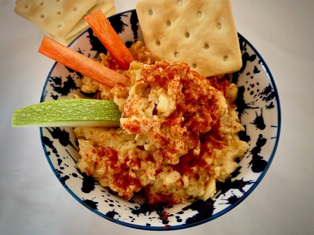 Bowl of chunky hummus with raw red pepper and gluten free cracker