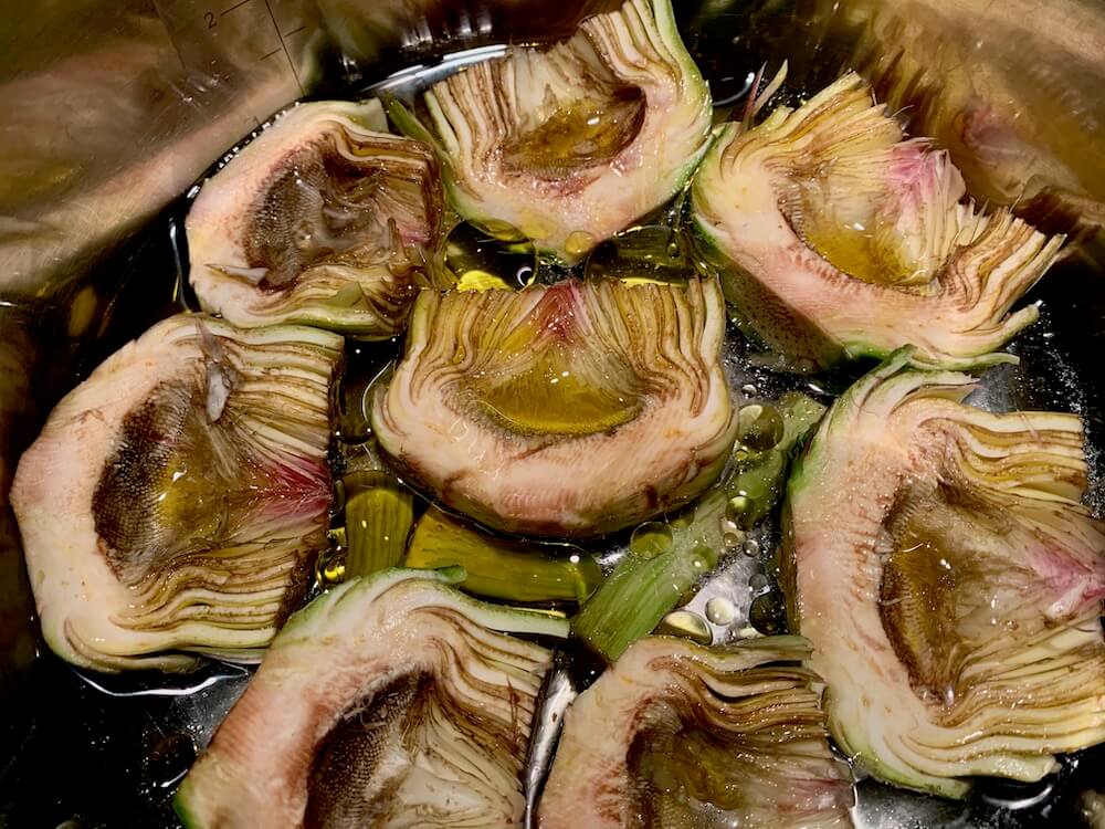 Raw artichokes in a pan with water and olive oil