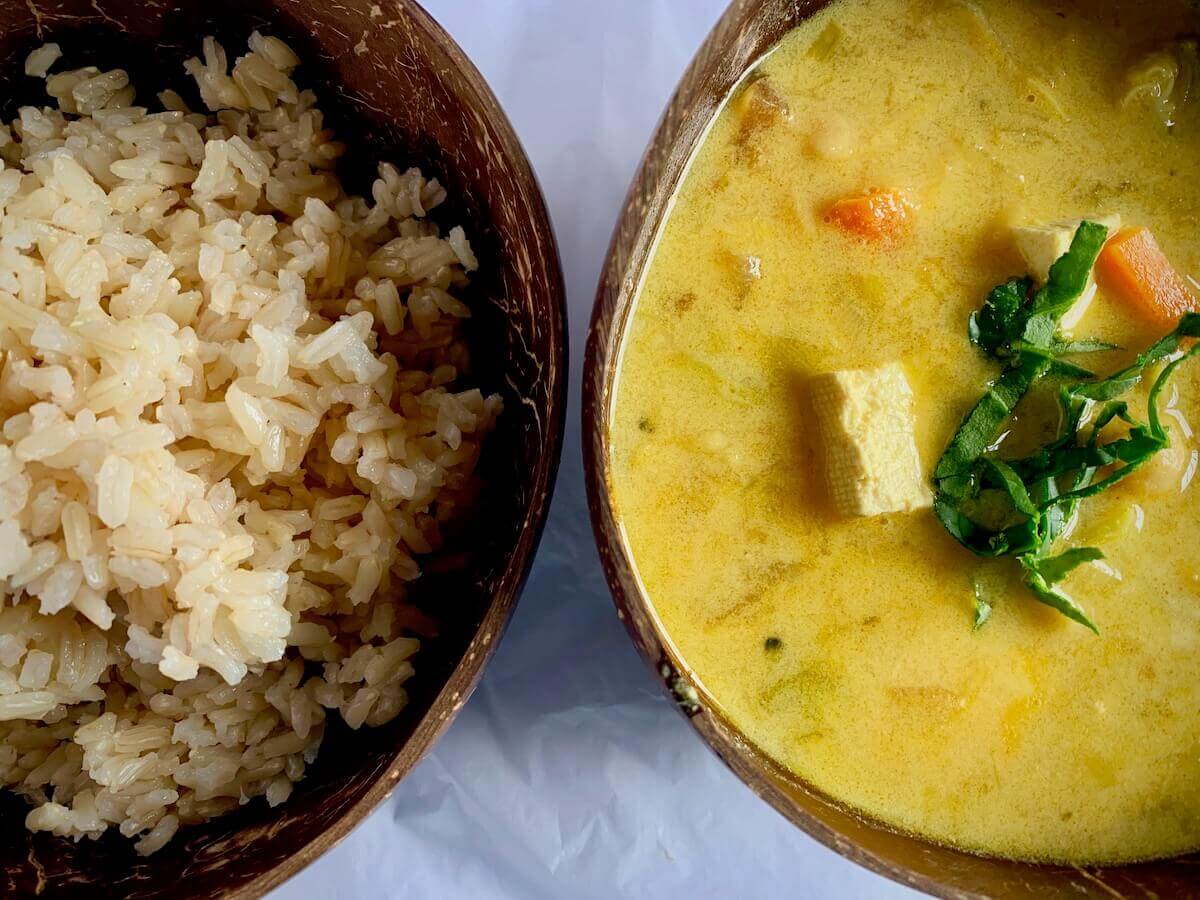 Two half bowls, one with rice, one with vegan coconut curry