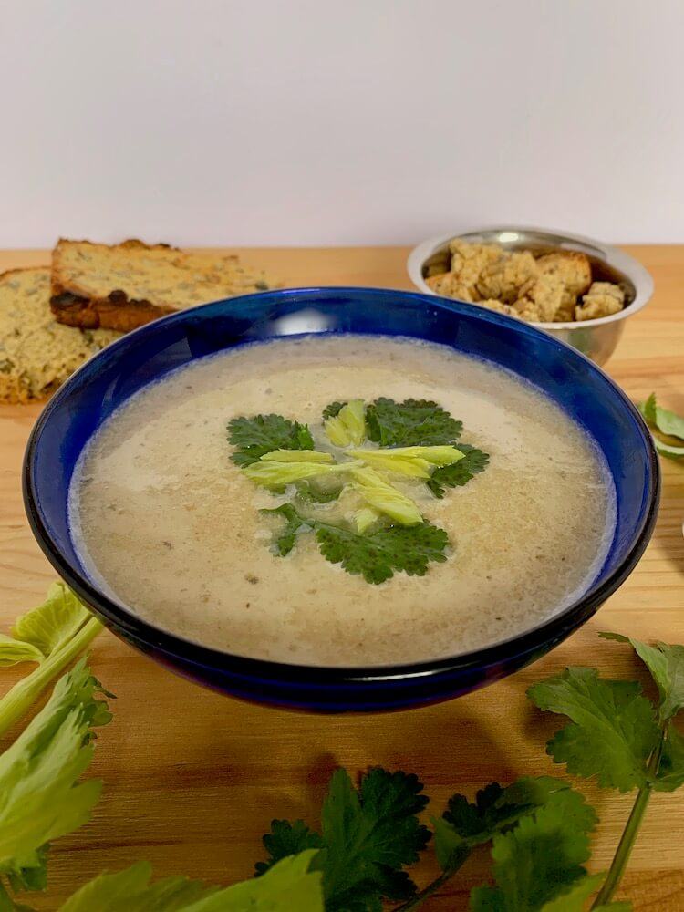Blue bowl of celery soup with garnish of coriander leaves and gluten free croutons