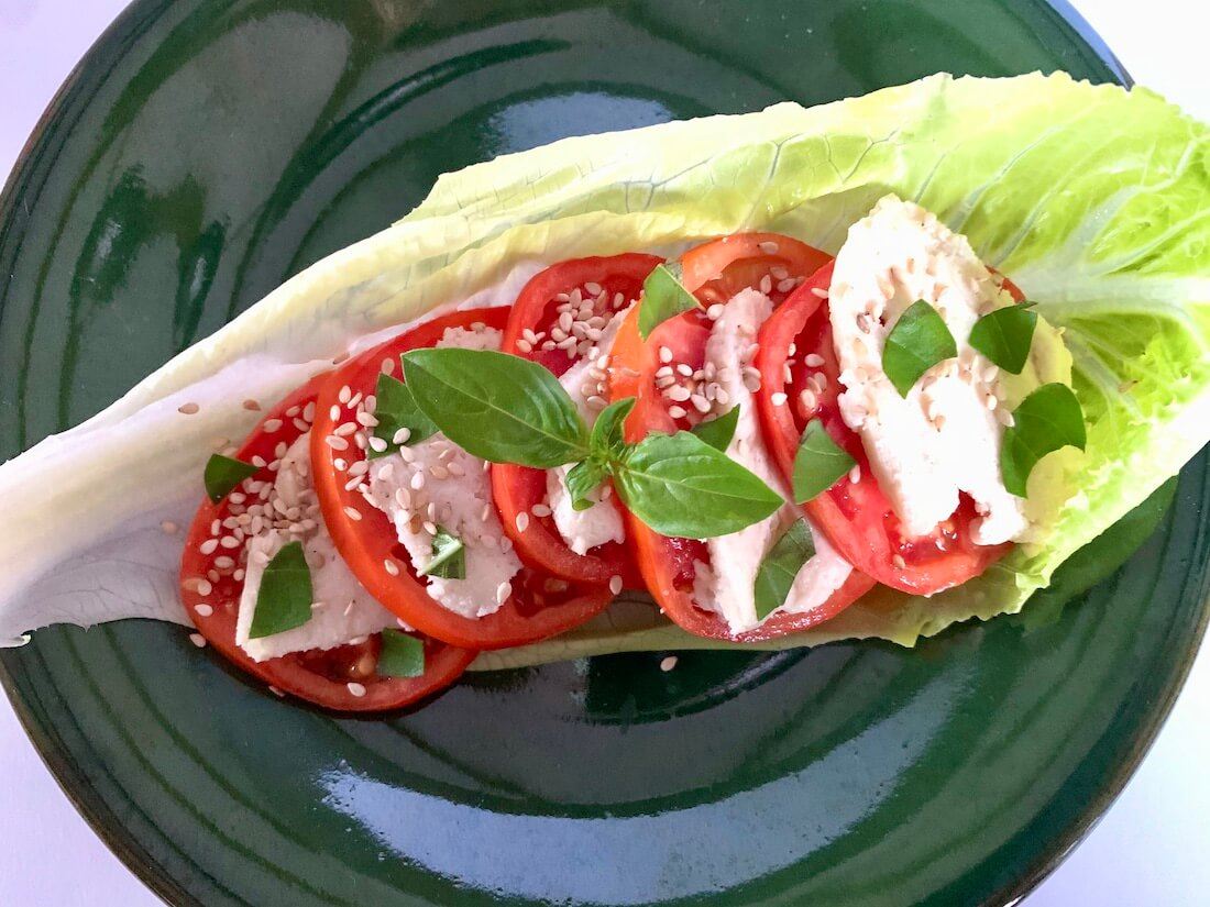 Lettuce leaf with slices of tomato and vegan mozzarella in it