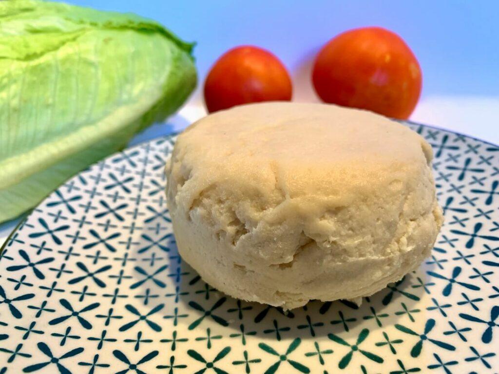 A whole vegan mozzarella with tomatoes and lettuce in the background