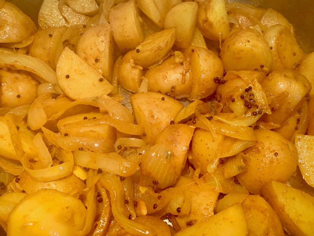 Close up of turmeric potatoes with black mustard seeds cooking in a pan