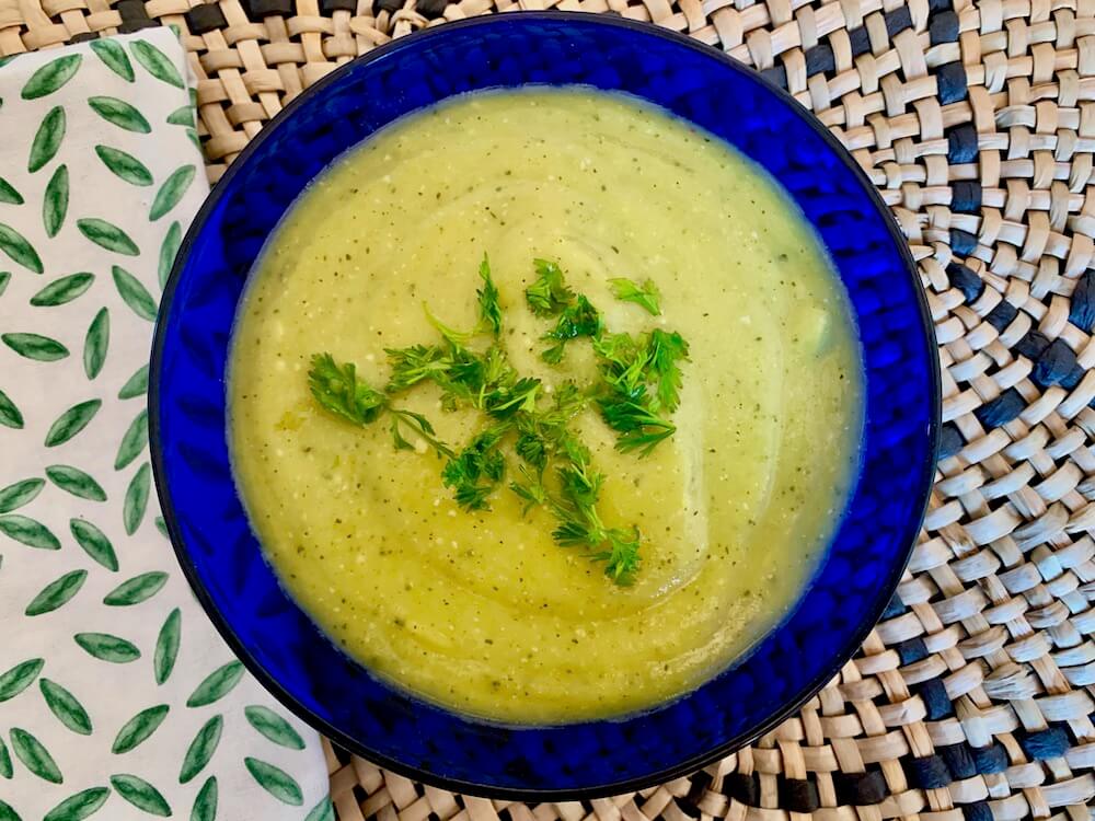 A blue bowl with zucchini soup and chopped coriander on top