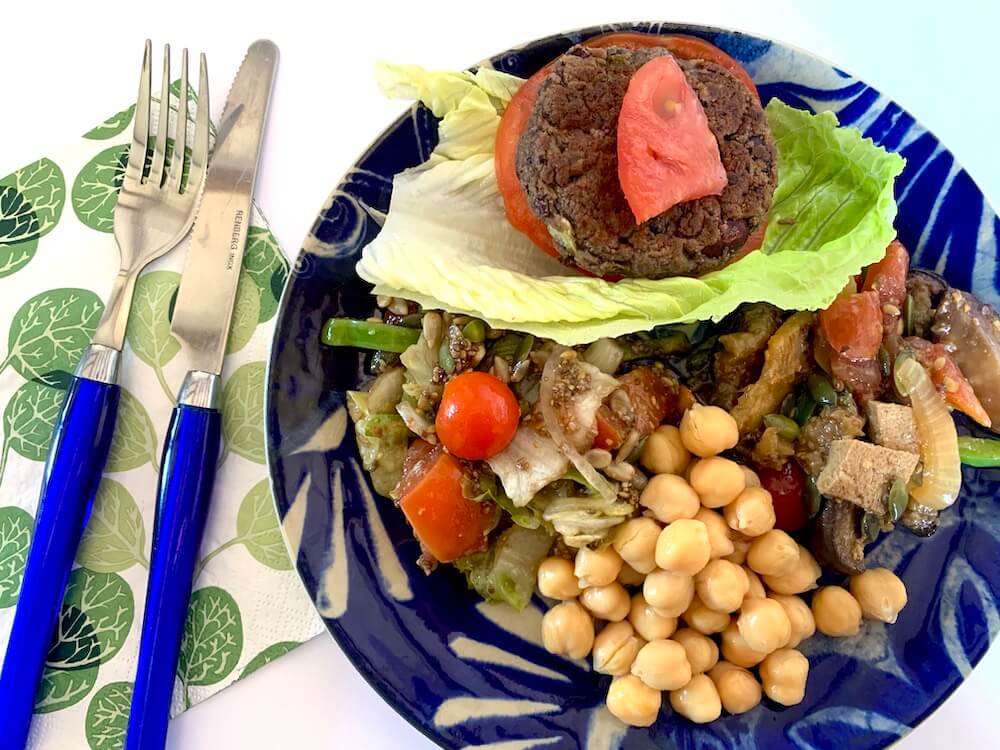 Easy vegan bean burger on a plate with salad, grilled veggies and chickpeas