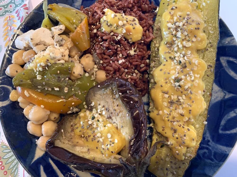 Close up of roast zucchini, eggplant, chickpea & pepper bake, red rice and vegan cheesy onion sauce
