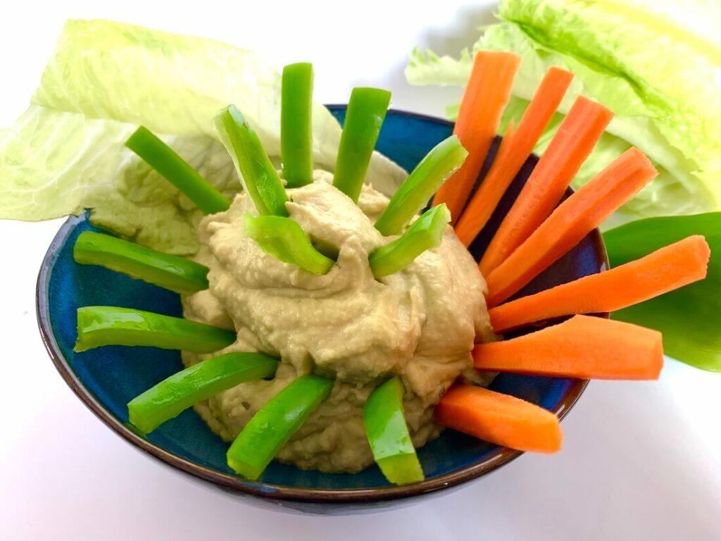 Bowl of avocado dip with crudités of green pepper and carrot sticking into it