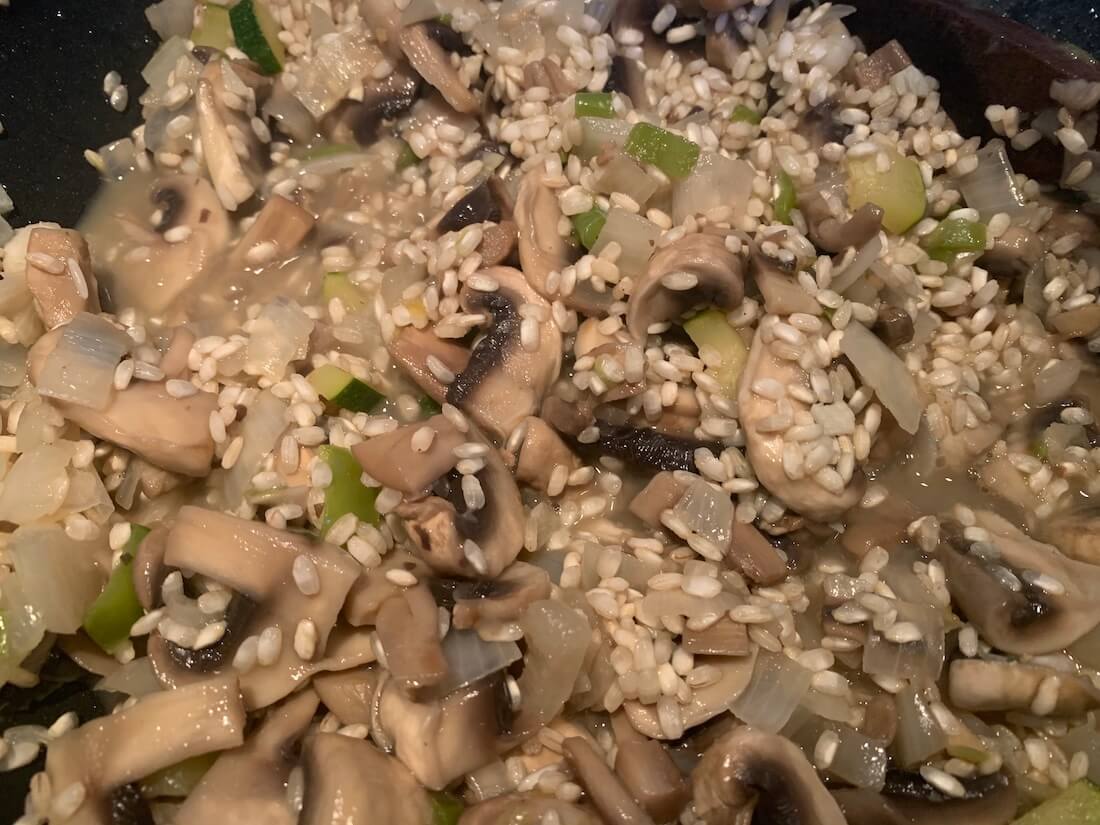 Raw rice added to the pan of mushrooms and onions