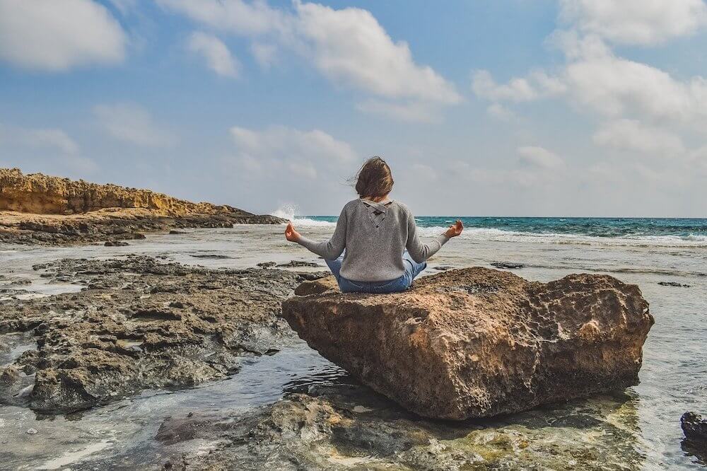 Girl sitting on a rock on the beach doing yoga