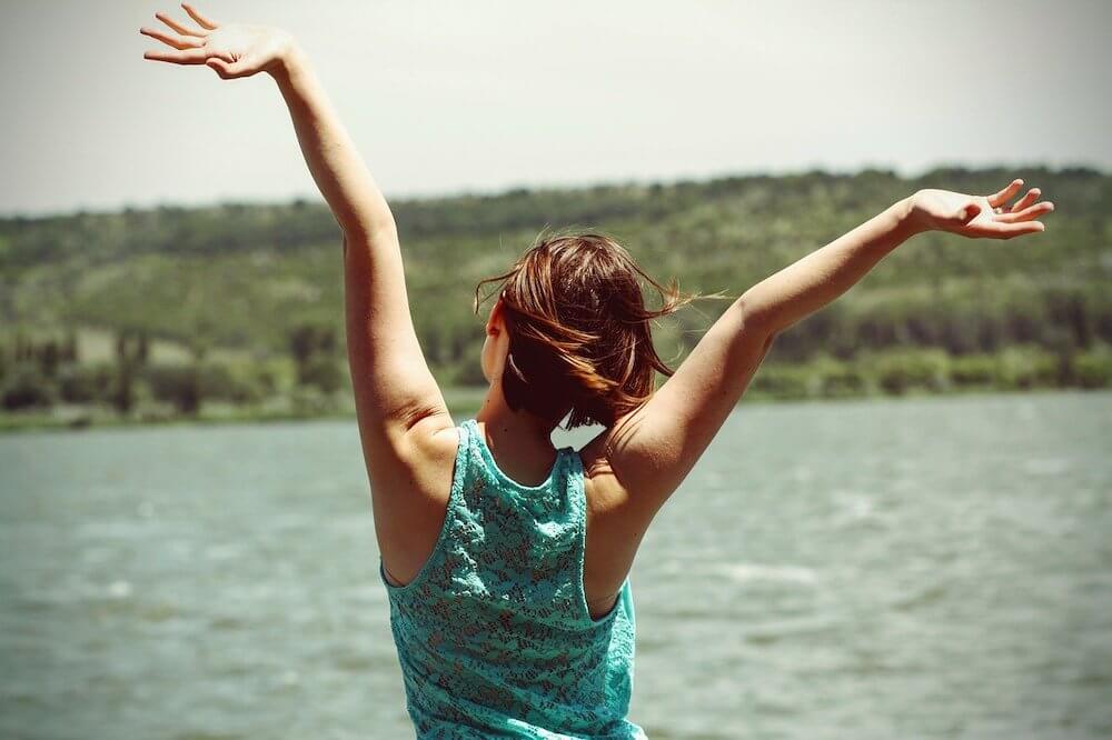 Woman facing away from camera with arms up in air in happiness