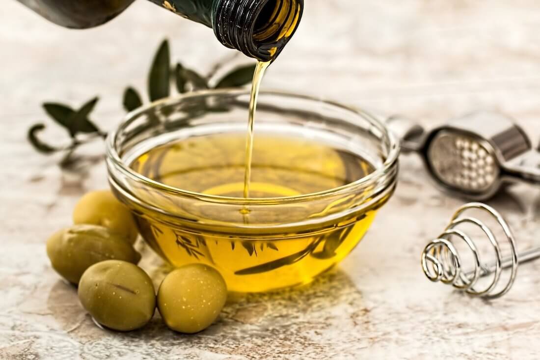 Bowl of olive oil with olives next to it