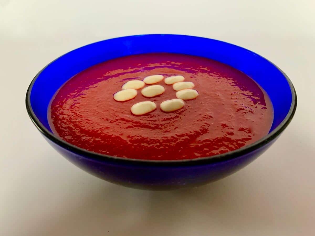 Blue bowl of beetroot soup with drops of vegan cream on top