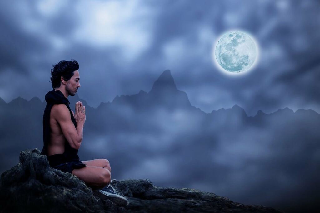 Man sitting meditating with mountains and the moon in the background