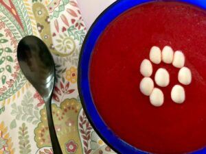 Close up showing half a blue bowl of beetroot soup with drops of vegan cream on top