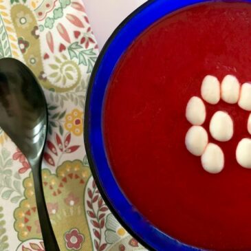 Close up showing half a blue bowl of beetroot soup with drops of vegan cream on top