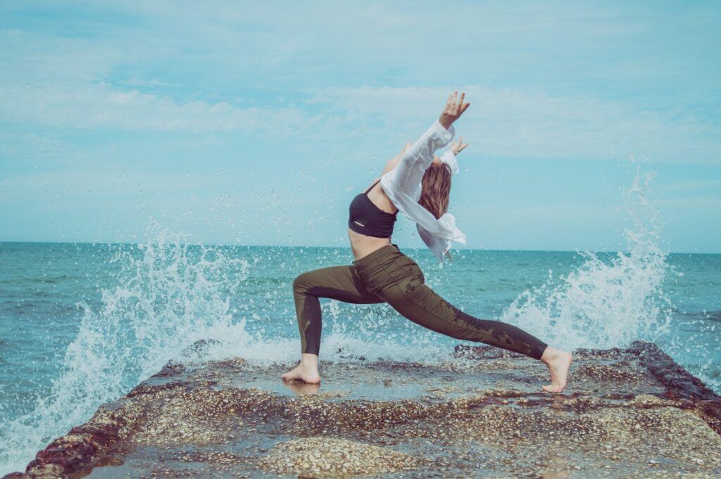 How to improve in yoga - woman doing yoga on a rock with sea spray behind