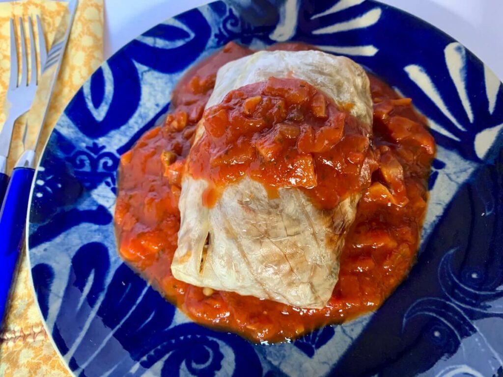 Vegan stuffed cabbage roll with tomato sauce served on a blue plate