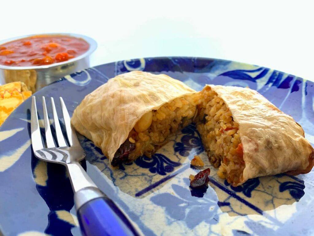 Vegan stuffed cabbage leaf cut in half with rice stuffing and tomato sauce in the background