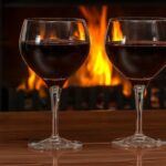 Two glasses of red wine in front of the fire