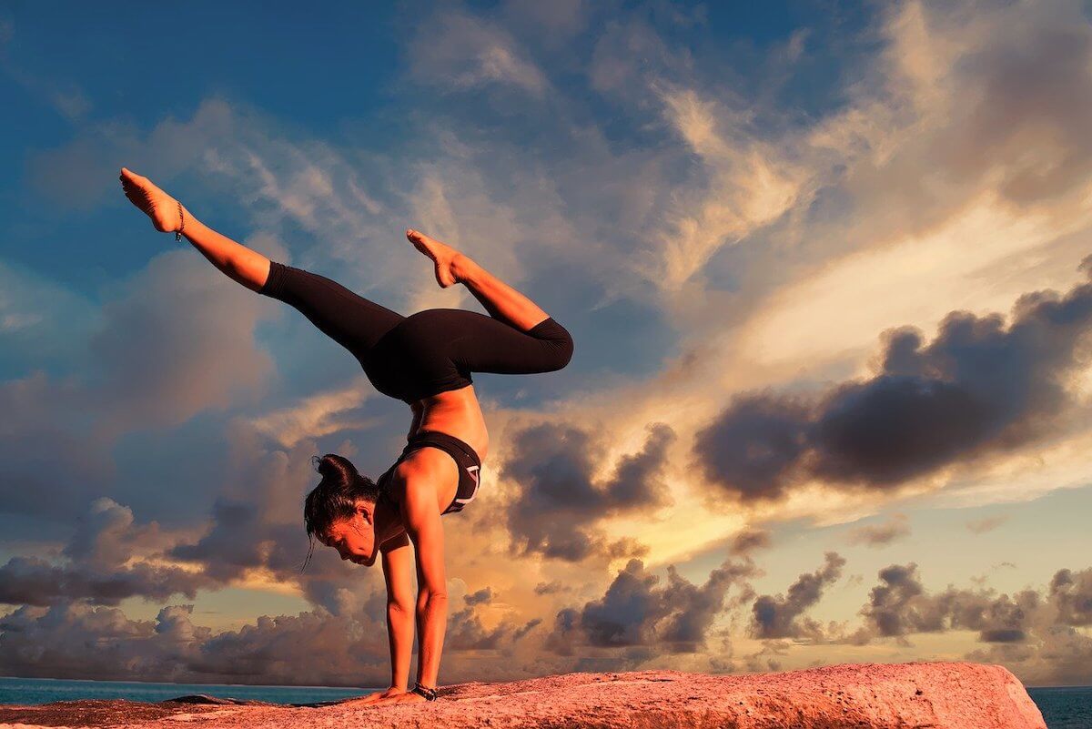 Woman doing yoga on a rock, with sky as a backdrop