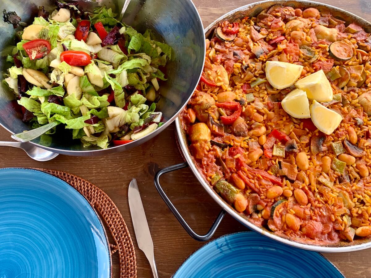 Vegan paella in a pan and a bowl of mixed salad