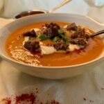 A bowl of roasted sweet potato & carrot soup topped with gluten free croutons, fresh cilantro and vegan cream