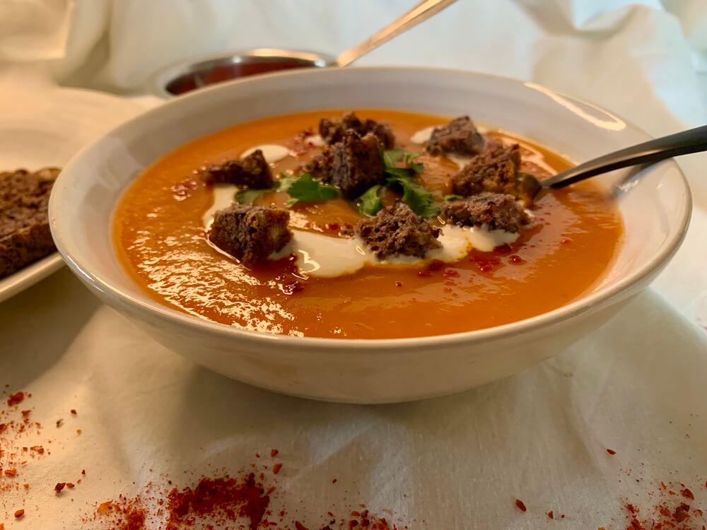 A bowl of roasted sweet potato can carrot soup topped with gluten free croutons, fresh cilantro and vegan cream