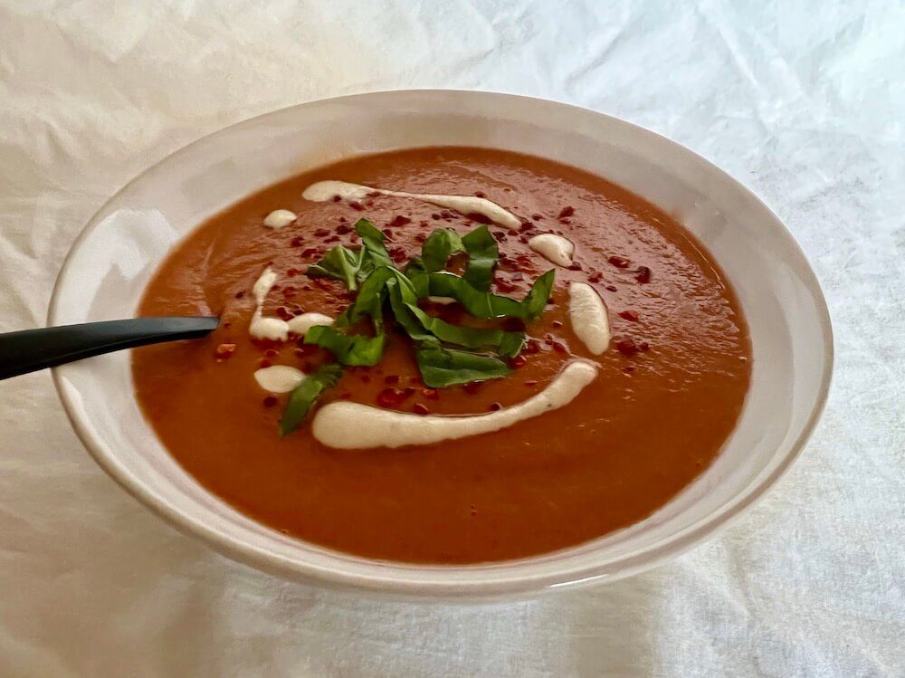 Simple roasted tomato soup recipe in a white bowl, topped with vegan cream and fresh basil