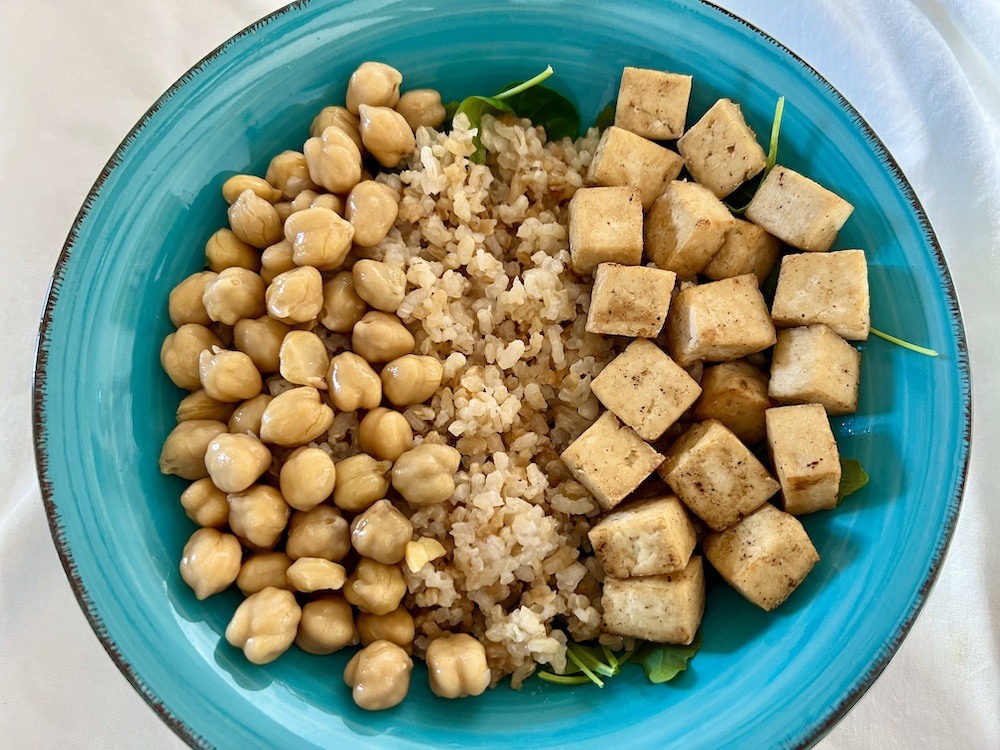 chickpeas and tofu on a bed of rice and green leaves