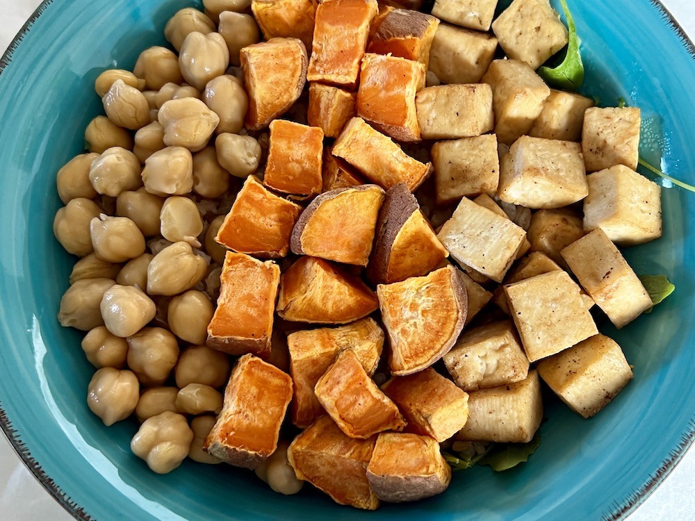 Chickpeas, sweet potato and tofu on a bed of rice and green leaves