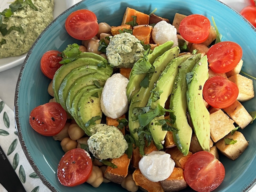 Favourite items for a vegan bowl - whole grain rice, green leaves, chickpeas, tofu, sweet potato, cherry tomato, avocado, cilantro pesto, cashew sauce, chopped cilantro