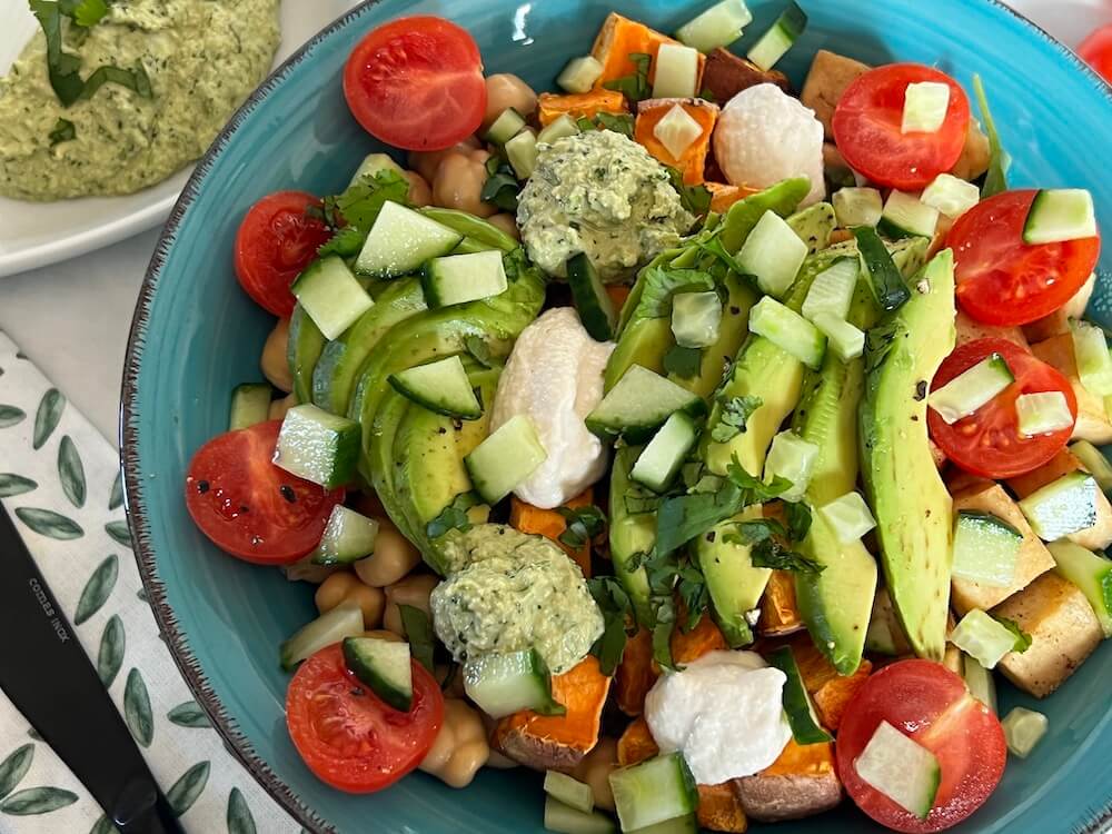 Vegan bowl with sweet potato, avocado, cherry tomatoes, cucumber, cashew sauce, cilantro sauce, rice and green leaves