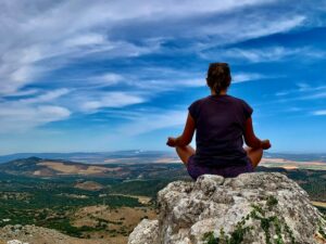 How to meditate on a question - person sitting cross legged on a rock, overlooking a view