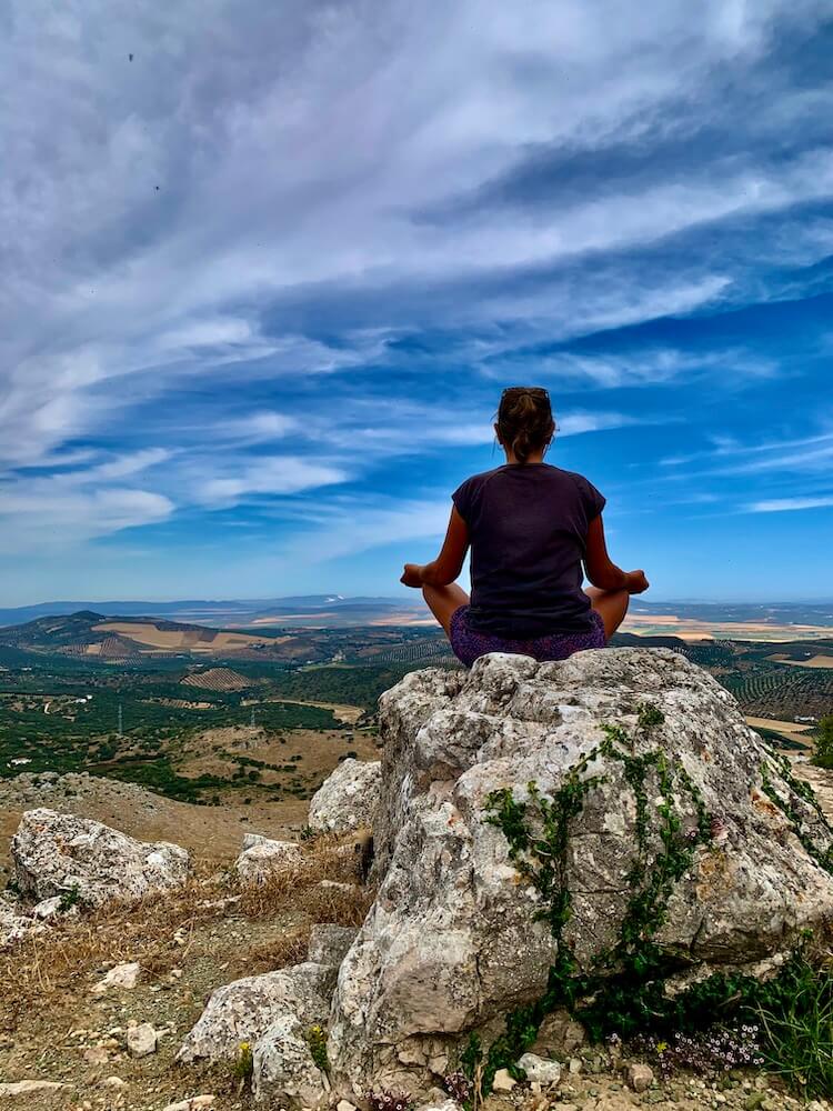 How to meditate on a question - person sitting cross legged on a rock, overlooking a far reaching view.