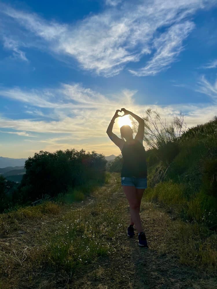 silhouette of someone creating a heart with their hands with the sunshine behind