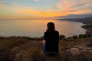 How long does it take to learn mindfulness? Person sitting looking out over the sea at sunset.
