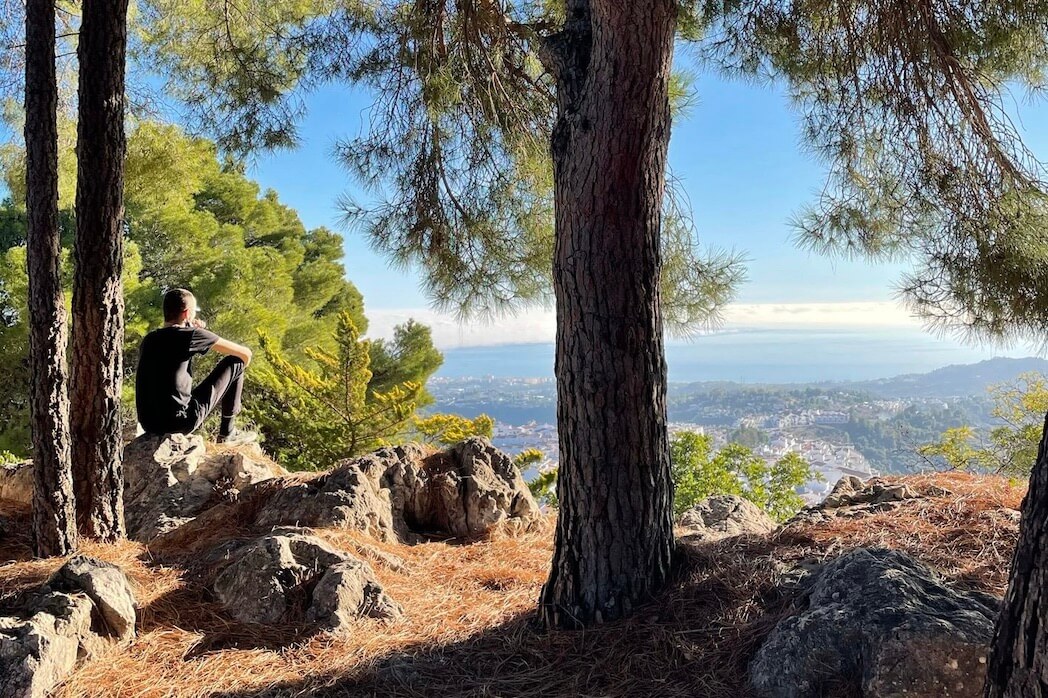 Relationship between mindfulness & a vegan diet. Person sitting on a rock in a forest, overlooking a distant view.