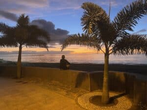 Should you set an alarm for meditating? Person sitting on a wall overlooking the sea, meditating.