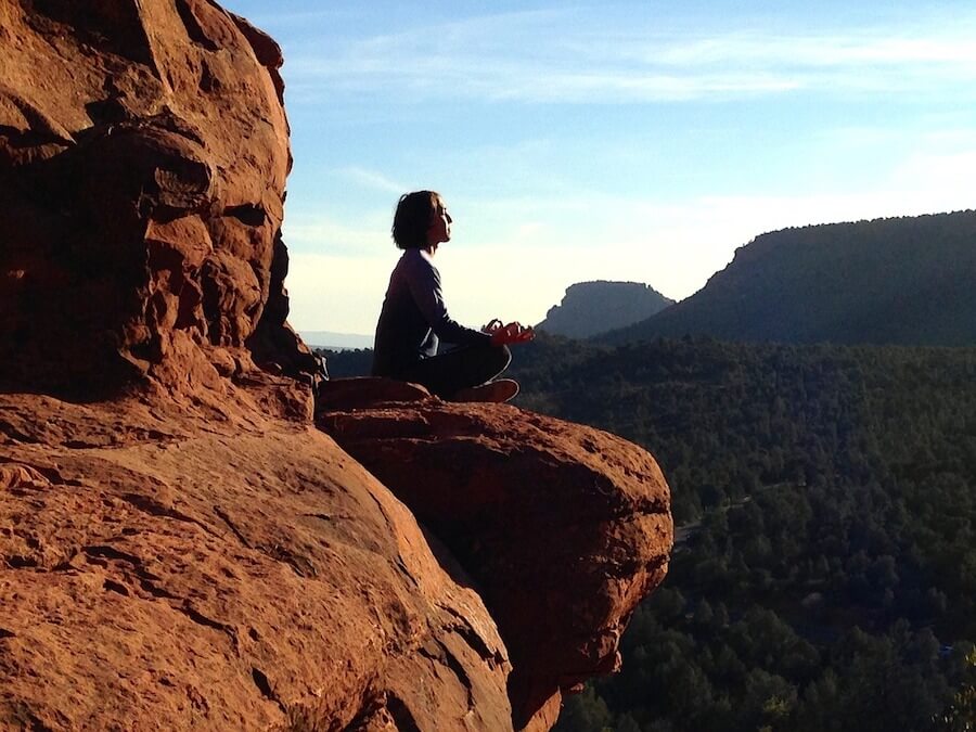 Do you think while meditating? Girl sitting high up on a red rock, over a forest and canyon