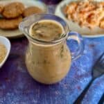 Vegan oil free mushroom gravy in a jug with food in the background