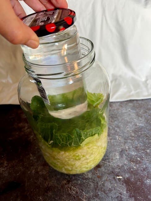 Sauerkraut in a mason jar with a smaller jar full of water to weigh it down.