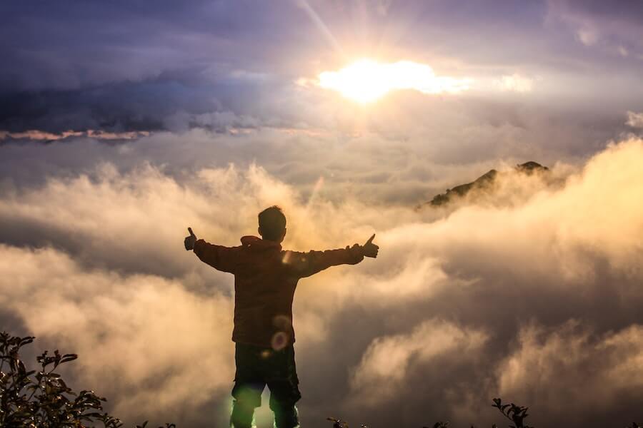 Man facing the clouds and the sunrise with arms outstretched in joy: vegan living