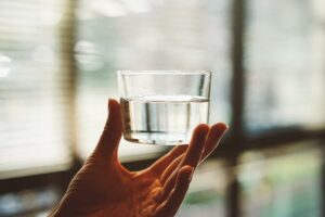 hand holding a glass of water against a background window - when do you stop feeling hungry on a water fast?