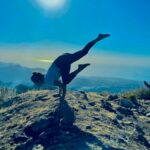 Aisha Perks arm balancing in nature with blue skies - Yogi Flight School review