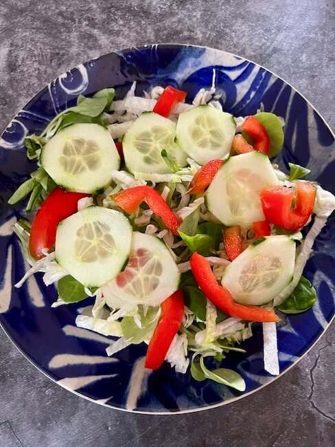 Bowl with green leaves, sliced cucumber and red pepper